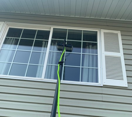 Water-fed pole cleaning a window on a home with vinyl siding