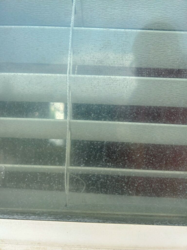 Close-up of hard water spots and mineral buildup on a window before cleaning
