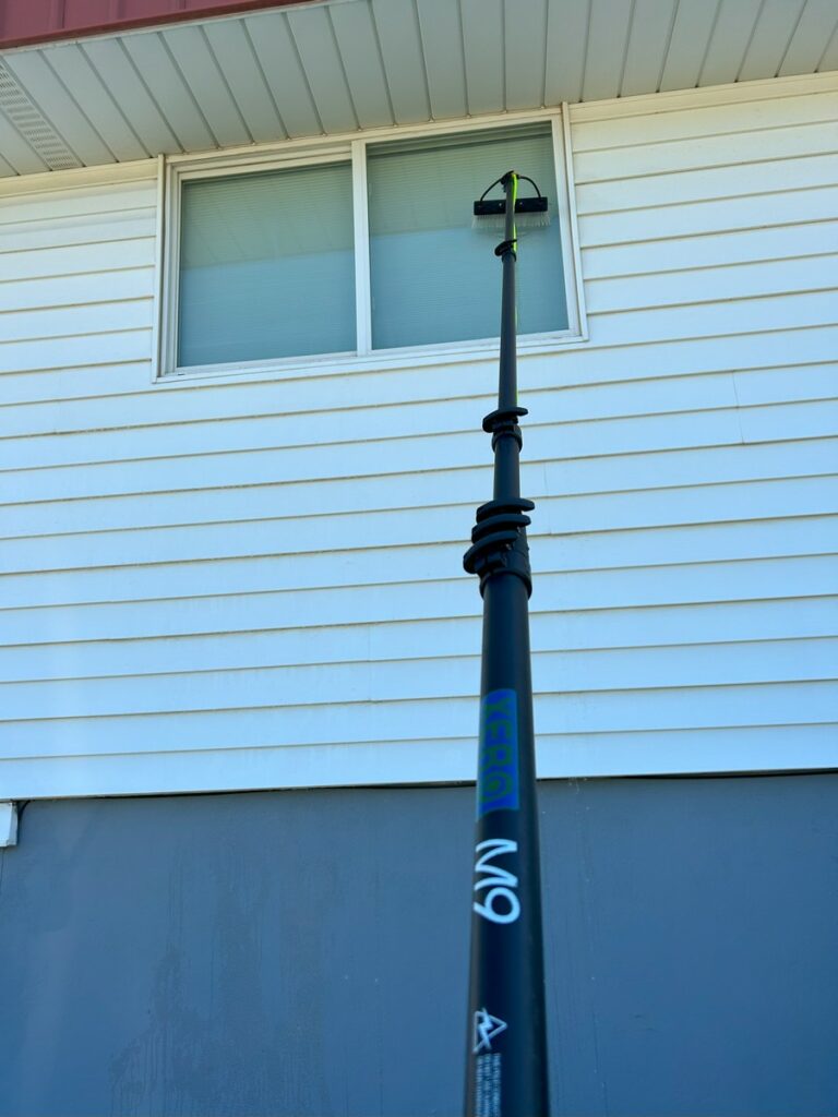 Extended water-fed pole reaching a second-story window on a home